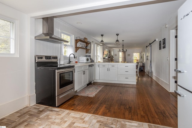 kitchen with white cabinets, wall chimney range hood, sink, appliances with stainless steel finishes, and kitchen peninsula