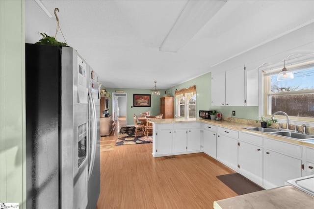 kitchen with white cabinetry, sink, stainless steel fridge with ice dispenser, kitchen peninsula, and pendant lighting