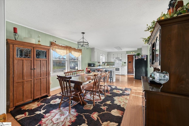 dining space with a notable chandelier, light wood-type flooring, and a textured ceiling