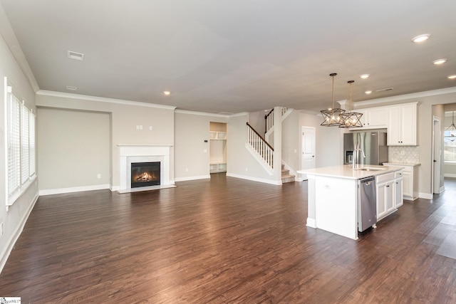 kitchen featuring appliances with stainless steel finishes, tasteful backsplash, a center island with sink, decorative light fixtures, and white cabinets