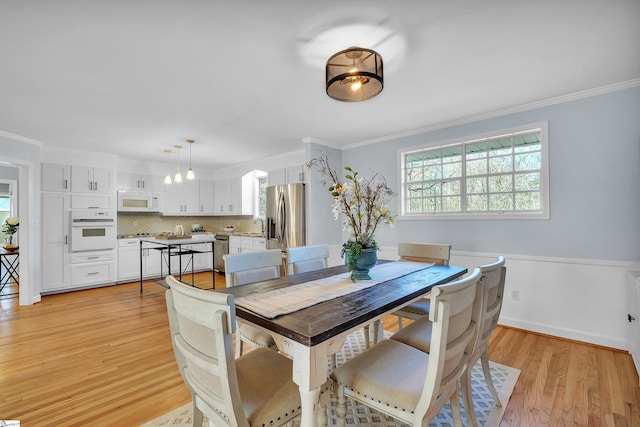 dining space with light wood-type flooring and ornamental molding