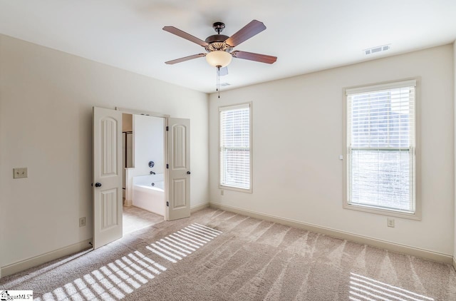 unfurnished bedroom with ensuite bathroom, ceiling fan, light carpet, and multiple windows