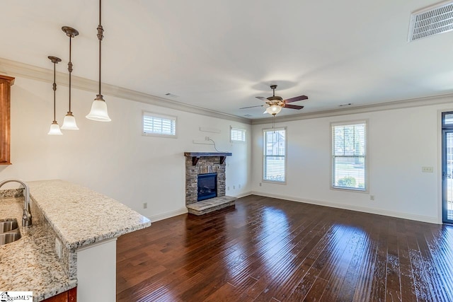 unfurnished living room with a fireplace, ceiling fan, sink, and a wealth of natural light