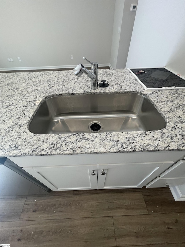 interior details with light stone counters, sink, dark wood-type flooring, and white cabinets