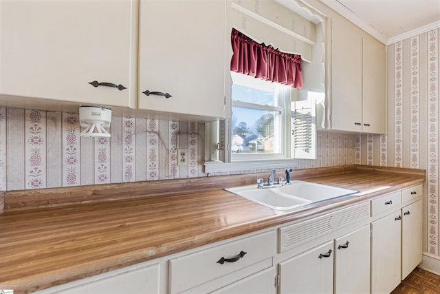 kitchen featuring white cabinets, crown molding, dark parquet flooring, and sink