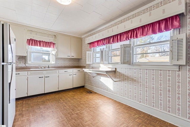 kitchen featuring a wealth of natural light, light parquet floors, white fridge, and sink