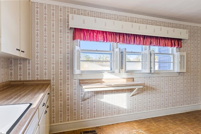 interior space featuring white cabinetry, sink, wooden counters, crown molding, and light parquet floors