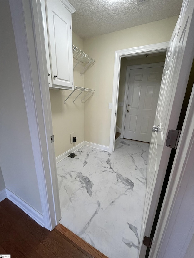 laundry area with hookup for an electric dryer, cabinets, and a textured ceiling