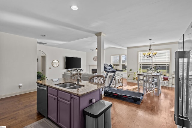 kitchen with stainless steel dishwasher, sink, decorative light fixtures, stone countertops, and an island with sink