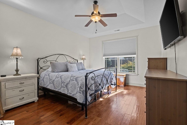 bedroom with ceiling fan, dark hardwood / wood-style floors, and a raised ceiling