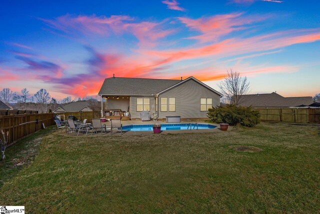 back house at dusk featuring a yard and a fenced in pool