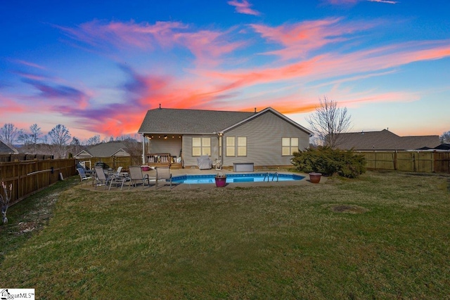 back house at dusk with a lawn and a fenced in pool