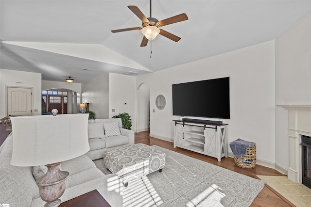 living room featuring a tile fireplace, ceiling fan, vaulted ceiling, and light wood-type flooring