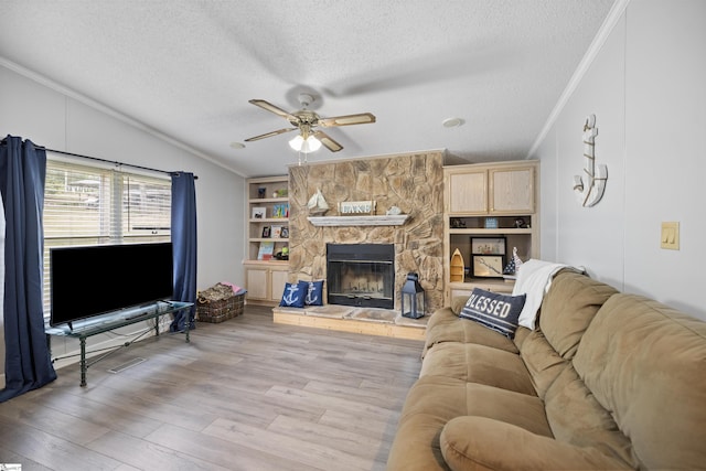 living room featuring light wood-type flooring, built in shelves, a textured ceiling, ceiling fan, and a fireplace