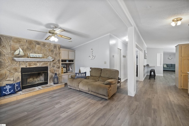 living room featuring ceiling fan, wood-type flooring, a textured ceiling, a fireplace, and ornamental molding