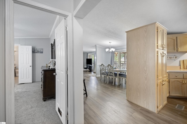 hall featuring crown molding, light hardwood / wood-style floors, a textured ceiling, and an inviting chandelier