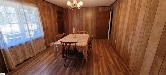 dining space featuring dark wood-type flooring, a notable chandelier, and wood walls