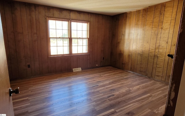 spare room featuring wooden walls, dark wood-type flooring, and a textured ceiling