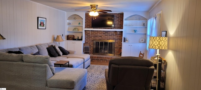 living room featuring built in shelves, ceiling fan, wooden walls, and a brick fireplace