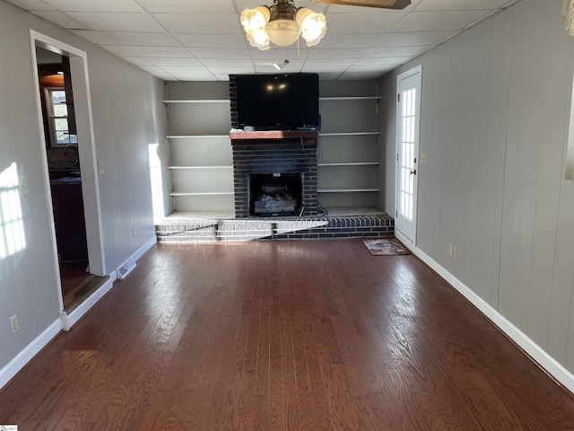 unfurnished living room with built in shelves, dark hardwood / wood-style flooring, a fireplace, and a drop ceiling