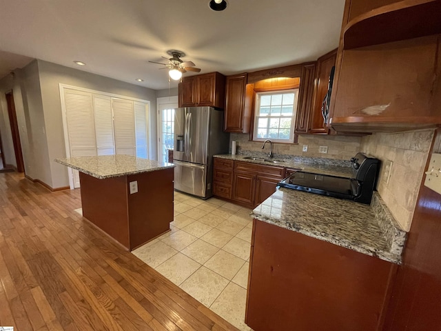 kitchen with a center island, black range with electric stovetop, sink, light stone countertops, and stainless steel fridge with ice dispenser