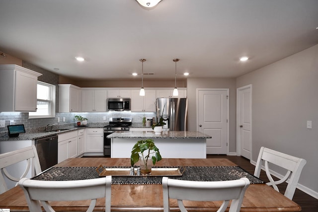 kitchen featuring white cabinets, decorative light fixtures, a kitchen island, and appliances with stainless steel finishes