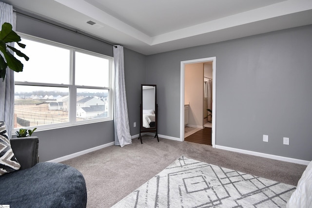 bedroom with ensuite bathroom, light carpet, and a tray ceiling