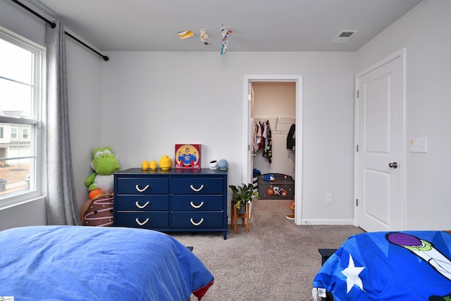 bedroom featuring a walk in closet, a closet, and light colored carpet