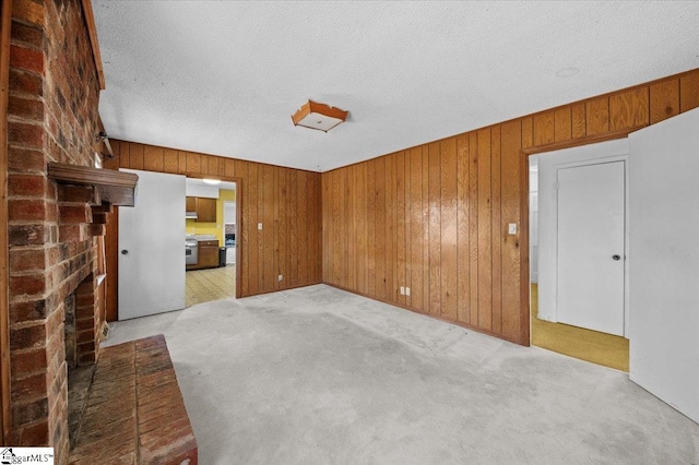 unfurnished living room featuring light carpet, a textured ceiling, a fireplace, and wooden walls