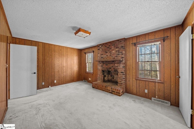 unfurnished living room featuring light carpet, a textured ceiling, a brick fireplace, and wood walls