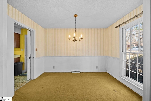 carpeted spare room featuring a textured ceiling and an inviting chandelier