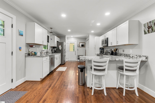 kitchen with kitchen peninsula, appliances with stainless steel finishes, white cabinetry, and a breakfast bar area