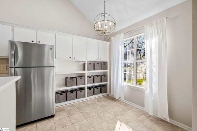 kitchen with hanging light fixtures, an inviting chandelier, stainless steel fridge, lofted ceiling, and white cabinets