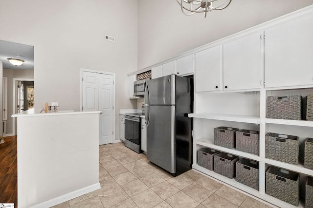 kitchen featuring kitchen peninsula, a towering ceiling, stainless steel appliances, light tile patterned floors, and white cabinets