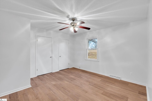 unfurnished bedroom featuring a textured ceiling, two closets, light hardwood / wood-style flooring, and ceiling fan