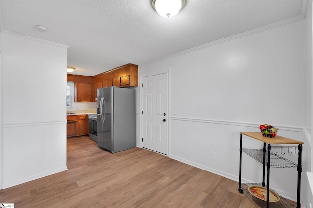 kitchen with a textured ceiling, crown molding, stainless steel appliances, and light hardwood / wood-style flooring