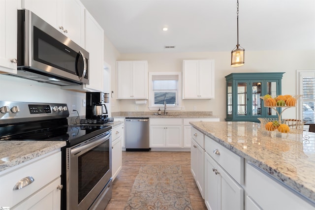 kitchen with light stone countertops, appliances with stainless steel finishes, pendant lighting, white cabinets, and light wood-type flooring