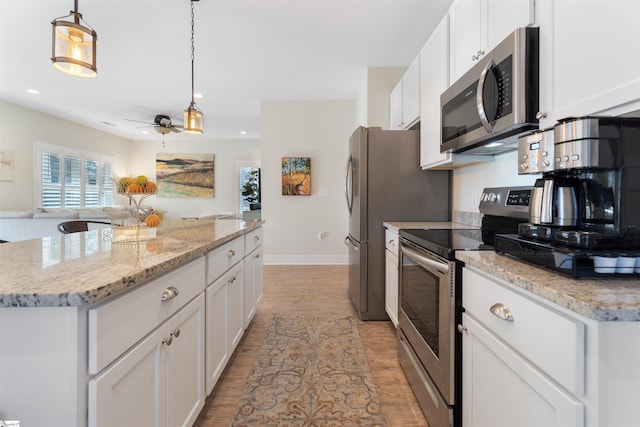 kitchen featuring stainless steel appliances, decorative light fixtures, a center island, light hardwood / wood-style floors, and white cabinetry