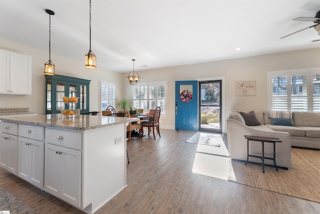 kitchen featuring pendant lighting, white cabinets, ceiling fan with notable chandelier, light stone countertops, and a breakfast bar area