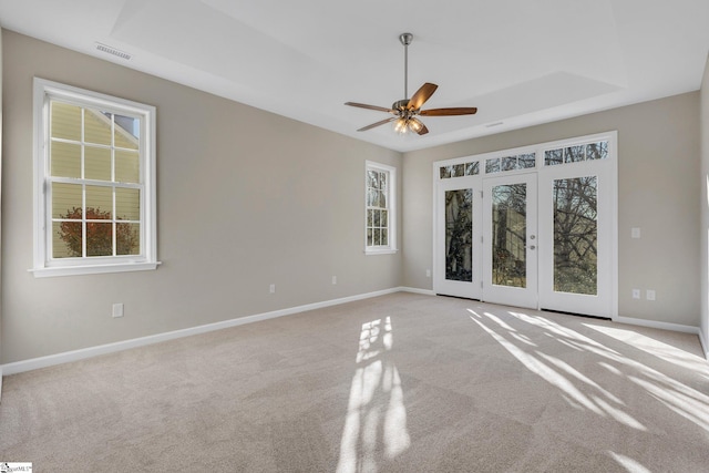 unfurnished room featuring a raised ceiling, ceiling fan, french doors, and light carpet