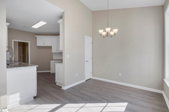 kitchen with white cabinetry, sink, light stone counters, a chandelier, and light wood-type flooring