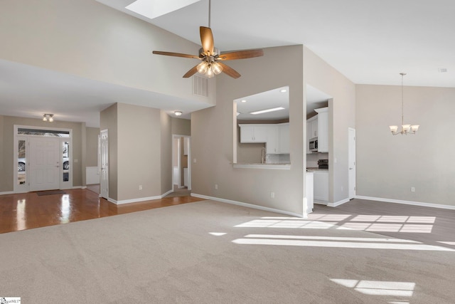 unfurnished living room with light carpet, ceiling fan with notable chandelier, and high vaulted ceiling