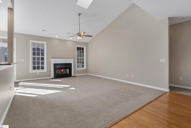 unfurnished living room with ceiling fan, vaulted ceiling with skylight, and light hardwood / wood-style floors