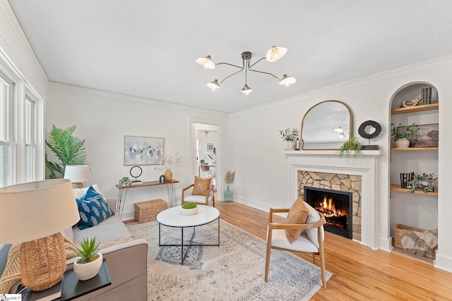 living room with built in shelves, crown molding, light hardwood / wood-style flooring, a notable chandelier, and a fireplace