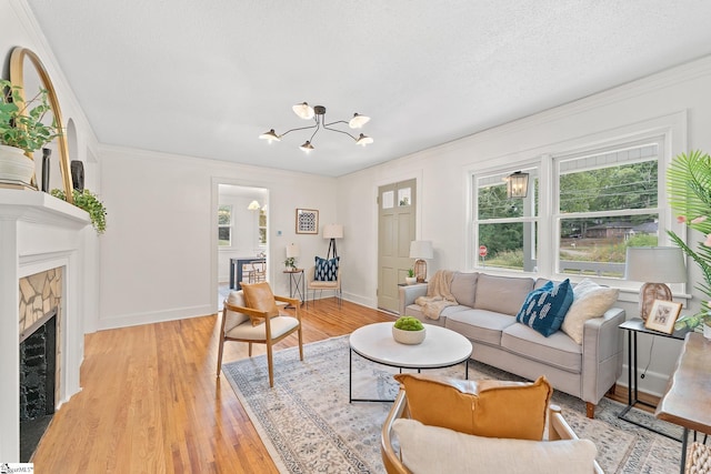 living room featuring a textured ceiling, crown molding, a notable chandelier, a fireplace, and light hardwood / wood-style floors