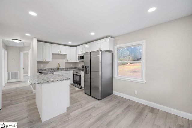 kitchen with sink, light stone countertops, appliances with stainless steel finishes, a kitchen island, and white cabinetry