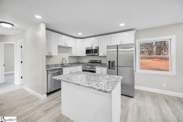 kitchen featuring light stone countertops, stainless steel appliances, sink, white cabinets, and a center island