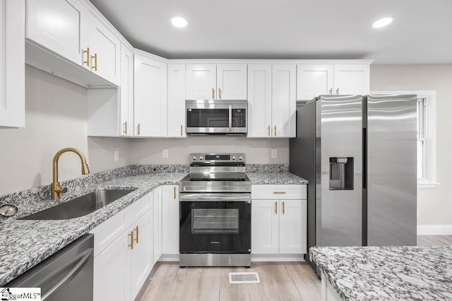 kitchen featuring sink, appliances with stainless steel finishes, light hardwood / wood-style floors, light stone counters, and white cabinetry