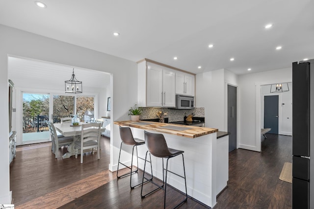 kitchen with white cabinets, kitchen peninsula, tasteful backsplash, a kitchen bar, and butcher block counters