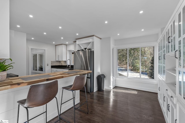 kitchen featuring tasteful backsplash, white cabinets, dark hardwood / wood-style floors, stainless steel refrigerator, and a breakfast bar area